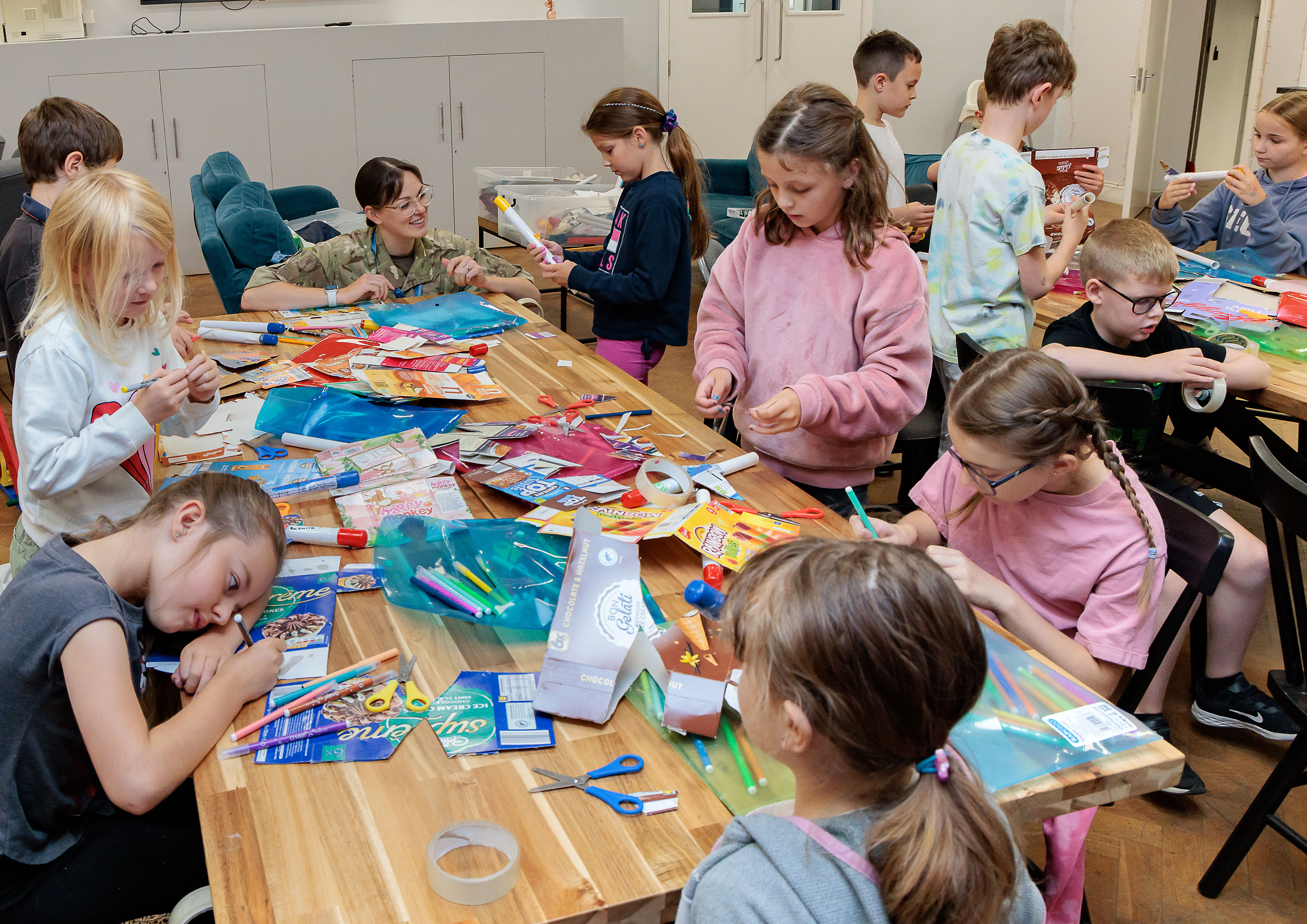 A group of 'Summer of STEM' students are seated and standing around tables, engaged in STEM activities, supported by Station's STEM ambassadors.